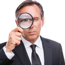 Businessman examining you. Serious mature man in formalwear examining you with magnifying glass while standing isolated on white background Businessman examining you. Serious mature man in formalwear examining you with magnifying glass while standing isolated on white background